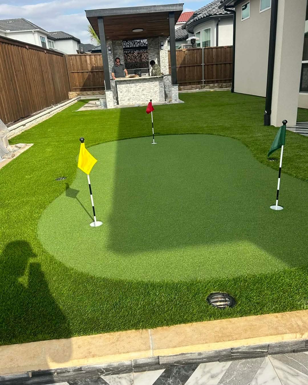 A backyard putting green with three flags, surrounded by artificial turf