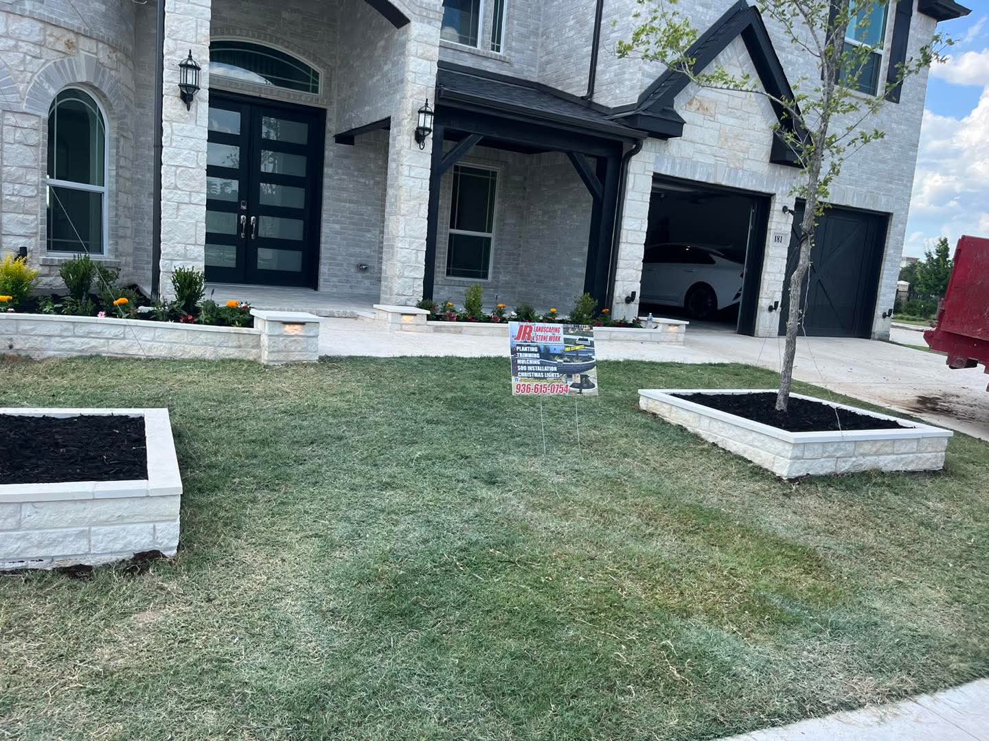 Raised white stone planters and lit stone beds across the front of a large limestone home